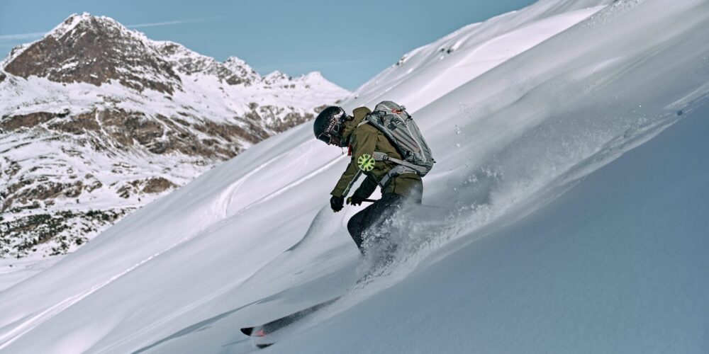 Skifahrer bei der Abfahrt durch Tiefschnee im Hintergrund Berge